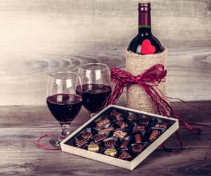 Bottle of wine, assorted box of chocolates, and two red wine glasses